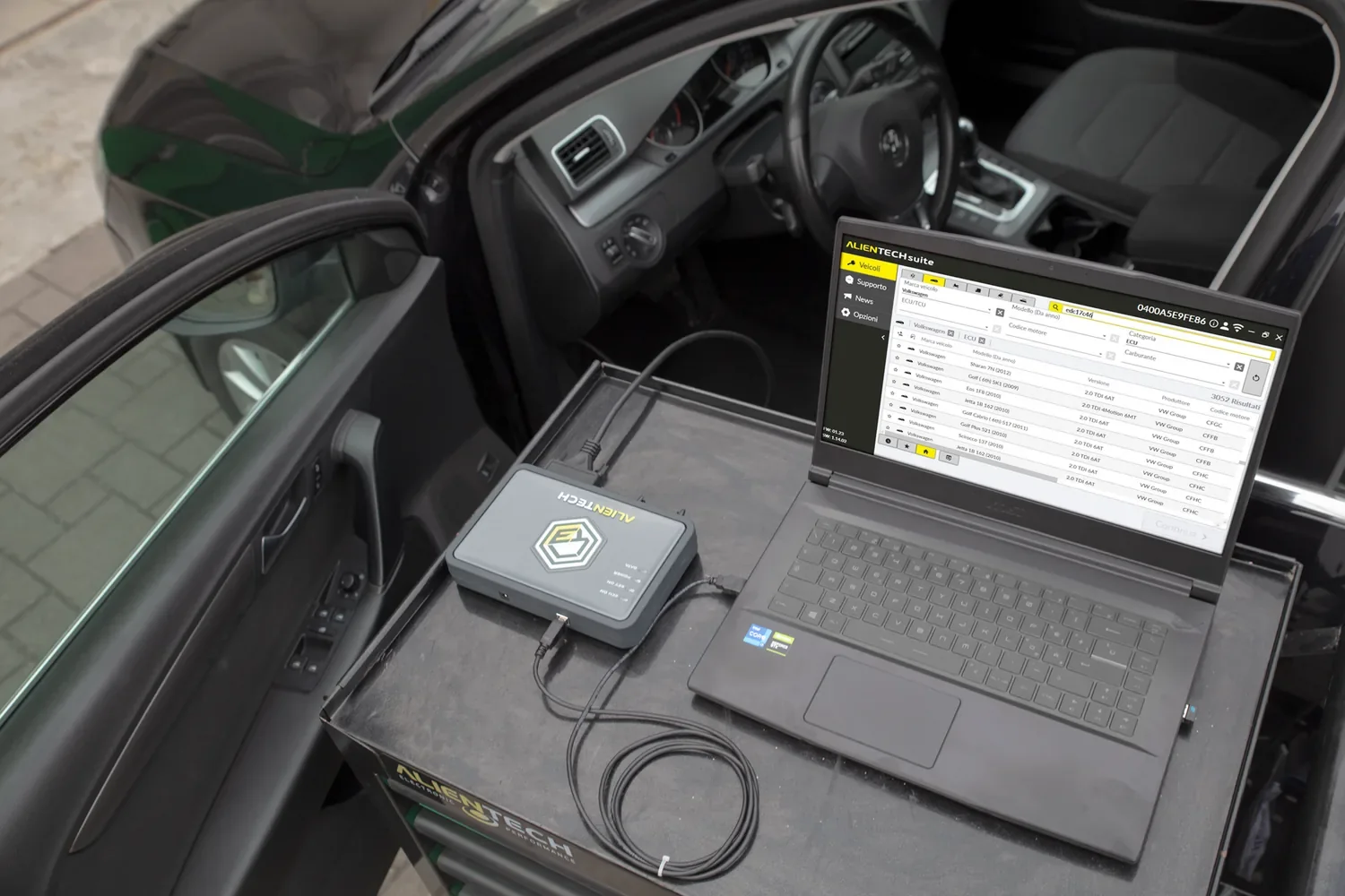 Un KESS3 Alientech relié à un ordinateur portable où tourne Alientech Suite, posé à la portière d'une voiture